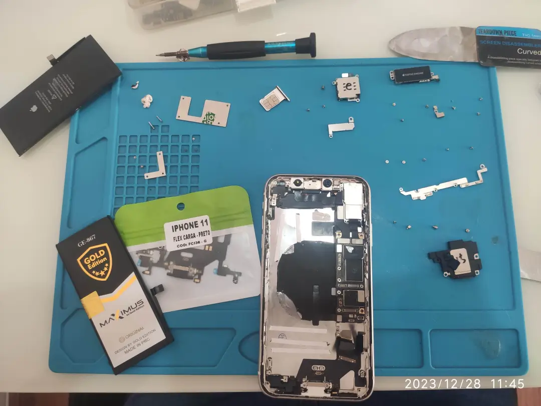 iPhone 11 desmontado, mostrando bateria e o conector de carga novo que será substituído no endereço do cliente.